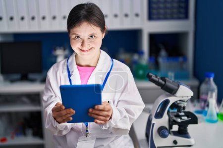 Foto de Mujer joven con síndrome de Down científico sonriendo confiado usando touchpad en el laboratorio - Imagen libre de derechos