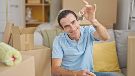 Foto de Hombre de mediana edad sosteniendo nuevas llaves de la casa sentado en el sofá en el nuevo hogar - Imagen libre de derechos