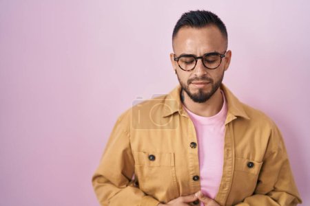 Photo for Young hispanic man standing over pink background with hand on stomach because indigestion, painful illness feeling unwell. ache concept. - Royalty Free Image