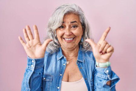 Téléchargez les photos : Femme d'âge moyen avec les cheveux gris debout sur fond rose montrant et pointant vers le haut avec les doigts numéro sept tout en souriant confiant et heureux. - en image libre de droit