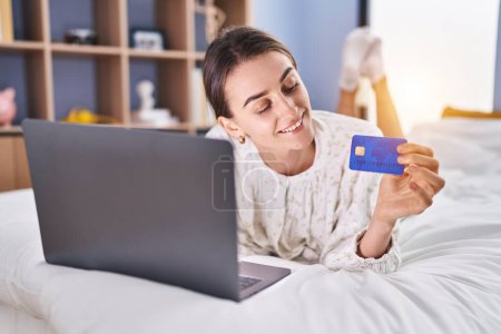Photo for Young caucasian woman using laptop and credit card sitting on bed at bedroom - Royalty Free Image