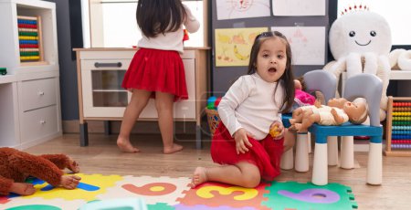 Téléchargez les photos : Adorable jumelles jouant repas avec cuisine et poupée de bébé à la maternelle - en image libre de droit