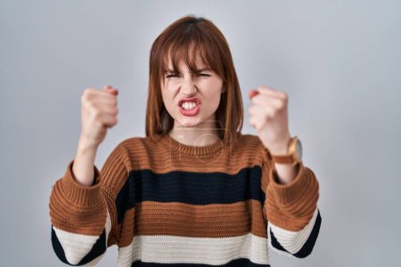 Photo for Young beautiful woman wearing striped sweater over isolated background angry and mad raising fists frustrated and furious while shouting with anger. rage and aggressive concept. - Royalty Free Image