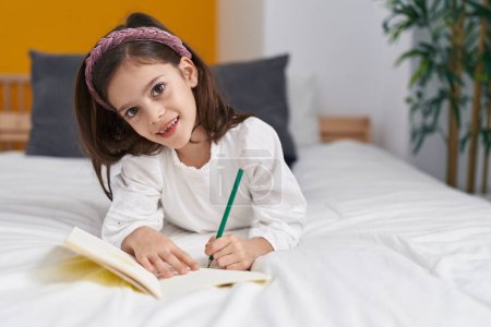 Téléchargez les photos : Adorable fille hispanique écrit sur ordinateur portable couché sur le lit dans la chambre - en image libre de droit
