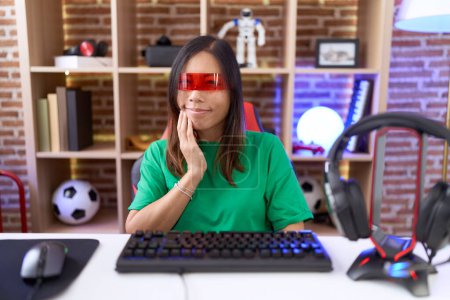 Photo for Middle age chinese woman wearing virtual reality glasses touching mouth with hand with painful expression because of toothache or dental illness on teeth. dentist - Royalty Free Image