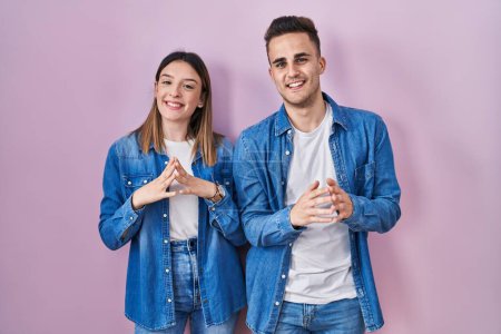 Foto de Joven pareja hispana de pie sobre el fondo rosa manos juntas y los dedos cruzados sonriente relajado y alegre. éxito y optimismo - Imagen libre de derechos