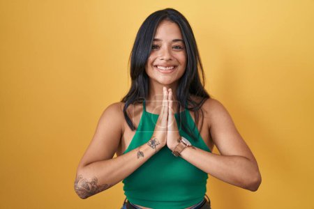 Photo for Brunette woman standing over yellow background praying with hands together asking for forgiveness smiling confident. - Royalty Free Image