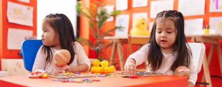 Photo for Adorable twin girls playing with maths puzzle game sitting on table at kindergarten - Royalty Free Image