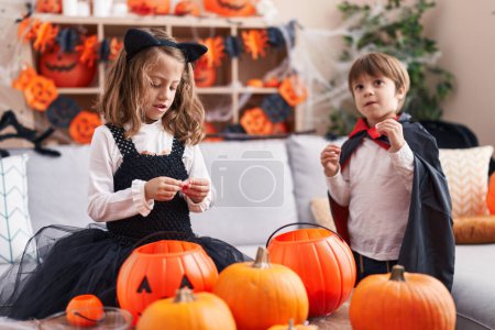 Foto de Adorable chico y chica teniendo fiesta de halloween comiendo dulces en casa - Imagen libre de derechos