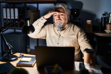 Foto de Hombre de mediana edad con el pelo gris trabajando en la oficina por la noche preocupado y estresado por un problema con la mano en la frente, nervioso y ansioso por la crisis - Imagen libre de derechos
