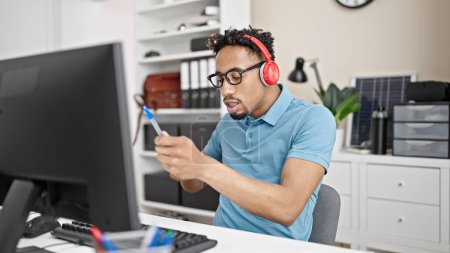 Téléchargez les photos : Homme d'affaires afro-américain écoutant de la musique faire un geste de batteur au bureau - en image libre de droit