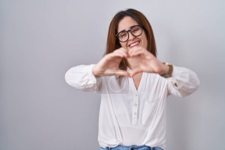 Photo for Brunette woman standing over white isolated background smiling in love doing heart symbol shape with hands. romantic concept. - Royalty Free Image