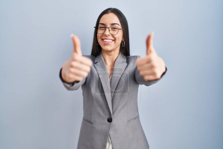 Foto de Mujer de negocios hispana con gafas aprobando hacer gesto positivo con la mano, pulgares arriba sonriendo y feliz por el éxito. gesto ganador. - Imagen libre de derechos