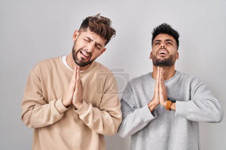 Photo for Young homosexual couple standing over white background begging and praying with hands together with hope expression on face very emotional and worried. begging. - Royalty Free Image