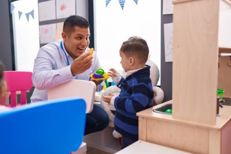 Photo for Hispanic man and boy playing with play kitchen standing at kindergarten - Royalty Free Image