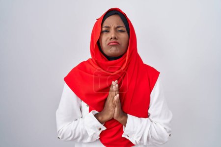 Photo for Young arab woman wearing traditional islamic hijab scarf begging and praying with hands together with hope expression on face very emotional and worried. begging. - Royalty Free Image