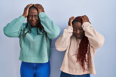 Photo for Two african woman standing over blue background suffering from headache desperate and stressed because pain and migraine. hands on head. - Royalty Free Image