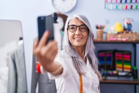 Photo for Middle age grey-haired woman tailor smiling confident make selfie by smartphone at tailor shop - Royalty Free Image