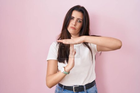 Photo for Young brunette woman standing over pink background doing time out gesture with hands, frustrated and serious face - Royalty Free Image
