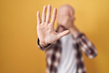 Photo for Hispanic man with beard standing over yellow background covering eyes with hands and doing stop gesture with sad and fear expression. embarrassed and negative concept. - Royalty Free Image