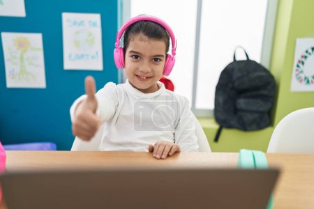 Téléchargez les photos : Adorable étudiante hispanique utilisant un ordinateur portable faisant geste pouce vers le haut à la salle de classe - en image libre de droit