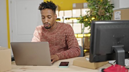 Téléchargez les photos : Homme afro-américain ecommerce travailleur d'affaires en utilisant ordinateur portable assis sur la table au bureau - en image libre de droit