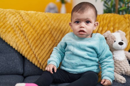 Photo for Adorable hispanic baby sitting on sofa with relaxed expression at home - Royalty Free Image