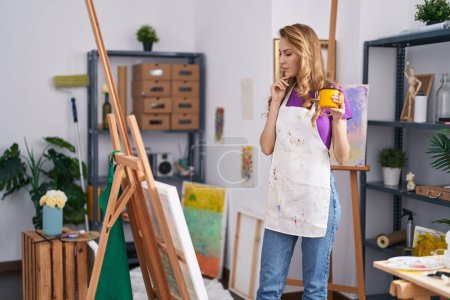 Téléchargez les photos : Jeune femme blonde artiste souriant confiance boire du café au studio d'art - en image libre de droit
