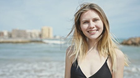 Téléchargez les photos : Jeune femme blonde touriste portant un bikini souriant à la plage - en image libre de droit