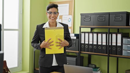 Téléchargez les photos : Jeune belle hispanique femme d'affaires travailleur souriant confiant tenant des documents au bureau - en image libre de droit