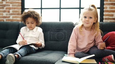 Photo for Adorable boy and girl students sitting on sofa drawing on notebook at home - Royalty Free Image