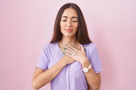 Téléchargez les photos : Young hispanic woman with long hair standing over pink background smiling with hands on chest with closed eyes and grateful gesture on face. health concept. - en image libre de droit