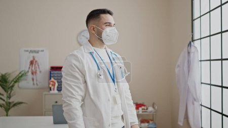 Photo for Young hispanic man doctor standing with serious expression wearing medical mask at clinic - Royalty Free Image