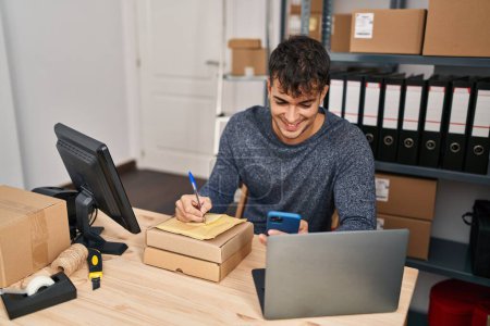 Foto de Joven hombre hispano comercio electrónico trabajador de negocios utilizando la escritura de teléfonos inteligentes en el paquete en la oficina - Imagen libre de derechos