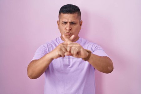 Téléchargez les photos : Jeune homme hispanique debout sur fond rose expression de rejet croisant les doigts faisant signe négatif - en image libre de droit