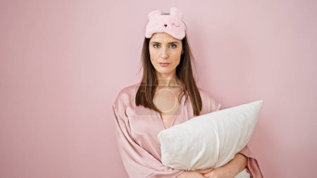 Téléchargez les photos : Jeune belle femme hispanique portant un masque de sommeil étreignant l'oreiller sur fond rose isolé - en image libre de droit