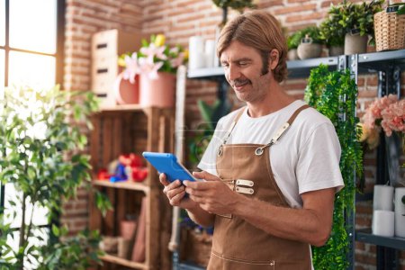 Téléchargez les photos : Young blond man florist smiling confident using touchpad at flower shop - en image libre de droit