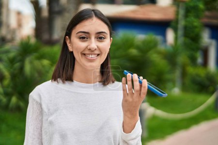 Téléchargez les photos : Jeune femme hispanique souriant confiant parler sur le smartphone au parc - en image libre de droit