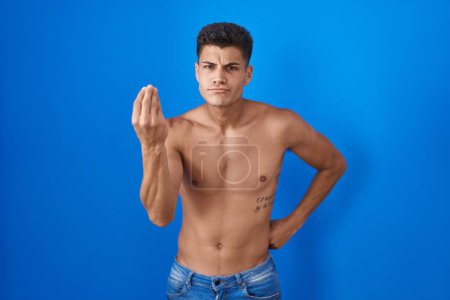 Foto de Joven hombre hispano de pie sin camisa sobre fondo azul haciendo gesto italiano con la mano y los dedos expresión de confianza - Imagen libre de derechos