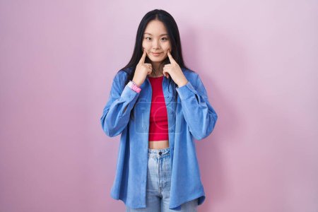 Téléchargez les photos : Jeune femme asiatique debout sur fond rose souriant avec la bouche ouverte, les doigts pointant et forçant sourire joyeux - en image libre de droit