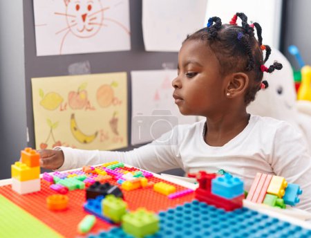 Foto de Chica afroamericana jugando con bloques de construcción sentados en la mesa en el jardín de infantes - Imagen libre de derechos