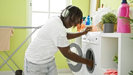 Téléchargez les photos : Afro-Américain écoutant de la musique laver les vêtements à la buanderie - en image libre de droit