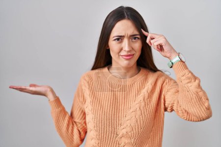 Photo for Young brunette woman standing over white background confused and annoyed with open palm showing copy space and pointing finger to forehead. think about it. - Royalty Free Image