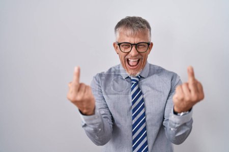 Foto de Hispanic business man with grey hair wearing glasses showing middle finger doing fuck you bad expression, provocation and rude attitude. screaming excited - Imagen libre de derechos