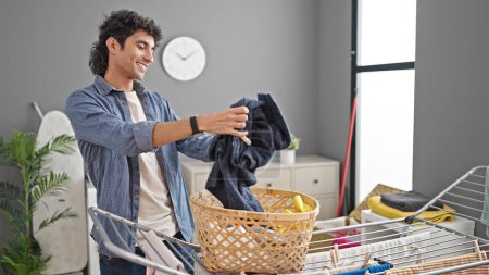 Photo for Young hispanic man hanging clothes on clothesline at laundry room - Royalty Free Image