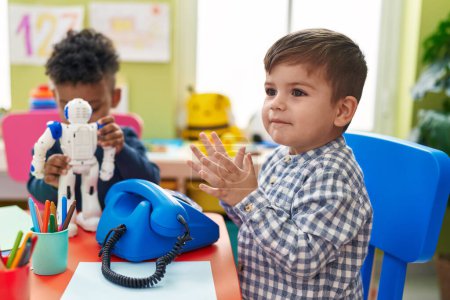 Téléchargez les photos : Adorables garçons jouant au téléphone et robot jouet assis sur la table à la maternelle - en image libre de droit