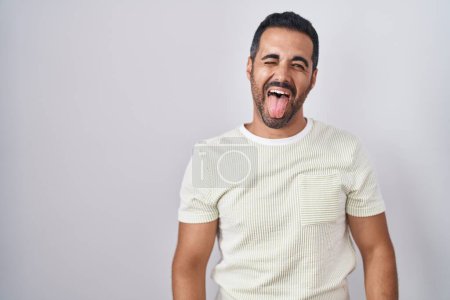 Téléchargez les photos : Homme hispanique avec barbe debout sur fond isolé langue collante heureux avec une expression drôle. concept d'émotion. - en image libre de droit