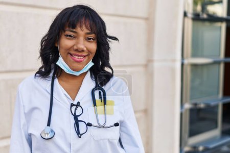 Téléchargez les photos : Médecin hispanique femme portant stéthoscope à l'extérieur regardant positif et heureux debout et souriant avec un sourire confiant montrant les dents - en image libre de droit