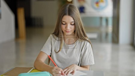 Foto de Joven chica hermosa estudiante escribiendo en cuaderno pensando en la biblioteca - Imagen libre de derechos