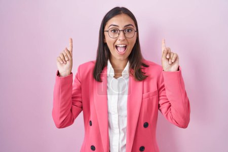 Photo for Young hispanic woman wearing business clothes and glasses smiling amazed and surprised and pointing up with fingers and raised arms. - Royalty Free Image